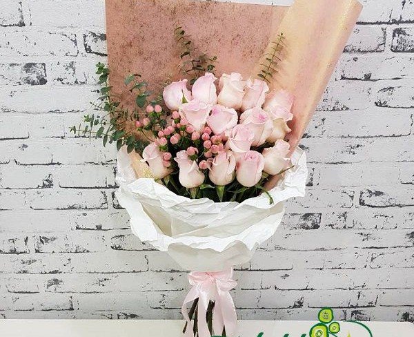 Букет из розовых роз, гиперикума и эвкалипта в белой бумаге с розовой лентой фото