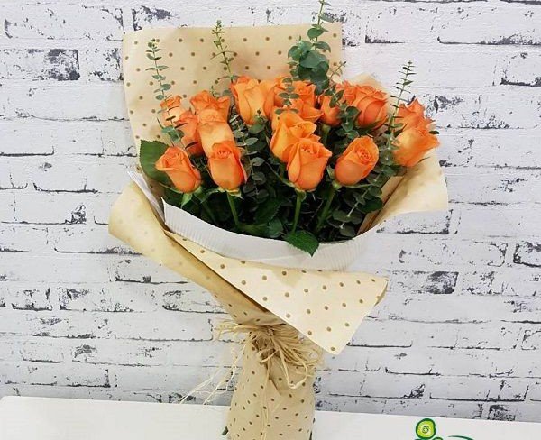 Букет из оранжевых роз и эвкалипта в крафт-бумаге в горошек фото
