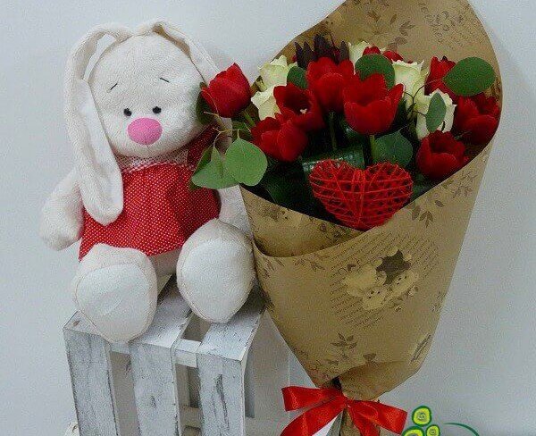 Букет из белых роз, красных тюльпанов, леукодендрона в крафт-бумаге и игрушка зайка фото