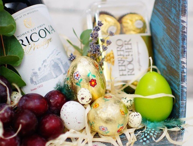Ящик с красным виноградом, бутылкой вина, конфетами, зеленой свечкой, декоративными яицами, эвкалиптом  фото