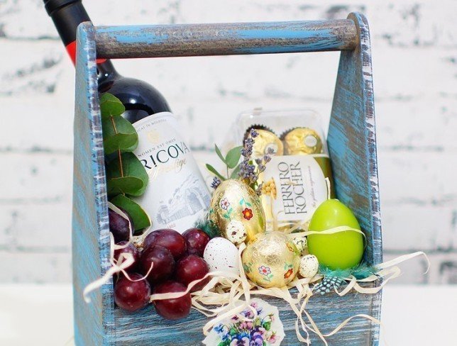 Ящик с красным виноградом, бутылкой вина, конфетами, зеленой свечкой, декоративными яицами, эвкалиптом  фото