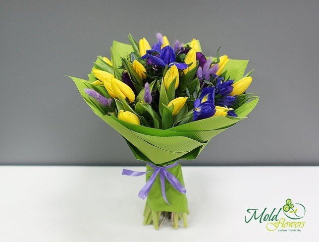 Bouquet of yellow tulips, spikelets, purple irises, eustoma in green paper photo