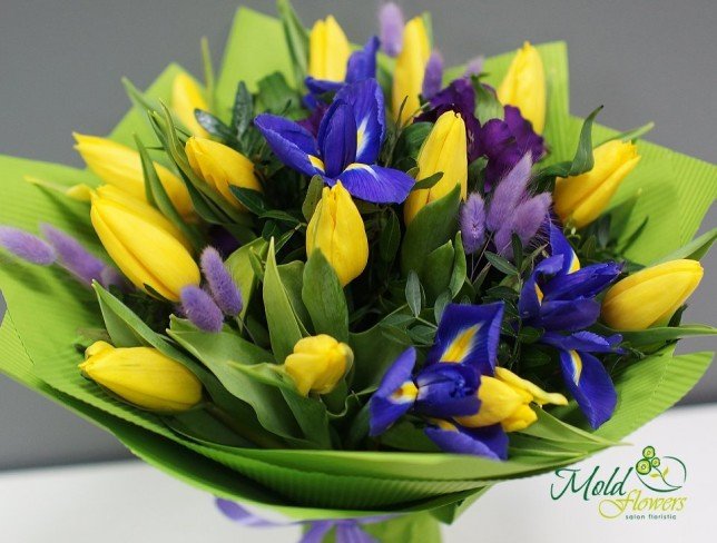 Bouquet of yellow tulips, spikelets, purple irises, eustoma in green paper photo