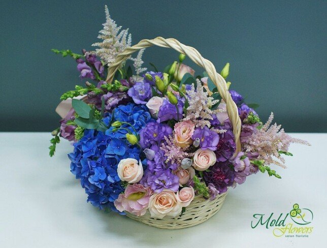 Composition with blue hydrangeas, pale pink roses, purple eustoma and pink astilbe, in a natural basket
