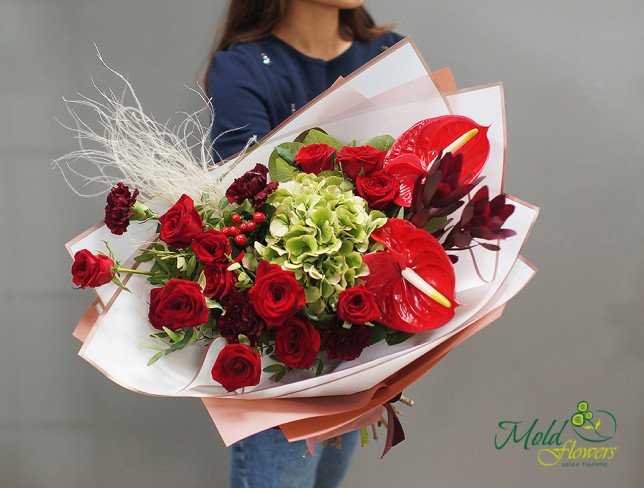 Bouquet of red roses, anthurium, green hydrangeas, and exotic leaves, wrapped in white and pink paper