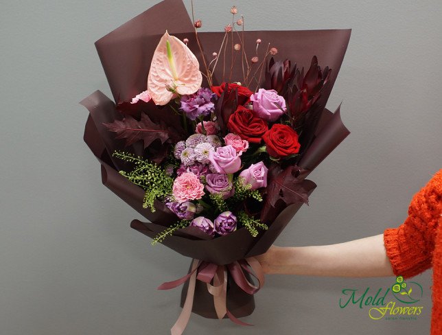 Bouquet with red and pink roses, pink anthuriums, carnations, tulips, purple chrysanthemums, scabiosa flowers, greenery, and burgundy leaves, wrapped in burgundy paper