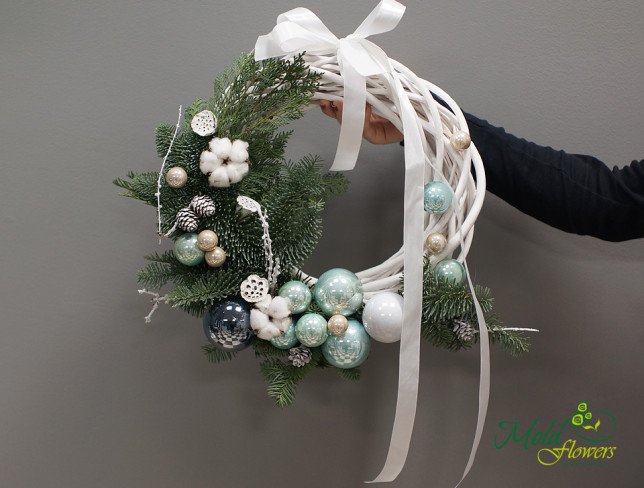 New Year’s wreath made of green fir branches, decorated with white and silver baubles, white pine cones, and cotton flowers