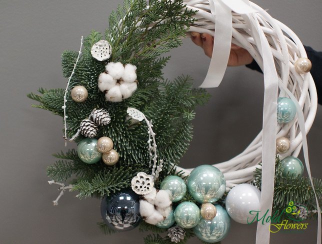 New Year’s wreath made of green fir branches, decorated with white and silver baubles, white pine cones, and cotton flowers