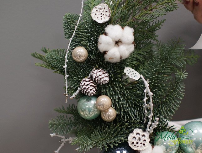 New Year’s wreath made of green fir branches, decorated with white and silver baubles, white pine cones, and cotton flowers